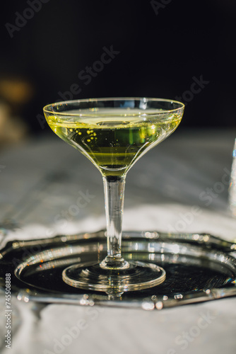 chartreuse green cocktail in coupe glass on silver tray, bed with dark background