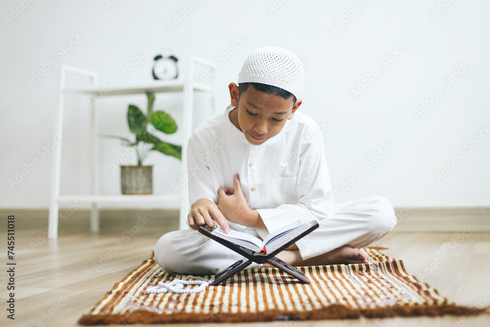 Asian muslim boy reading Quran on prayer mat at home Asian muslim boy reading Quran on prayer mat at home