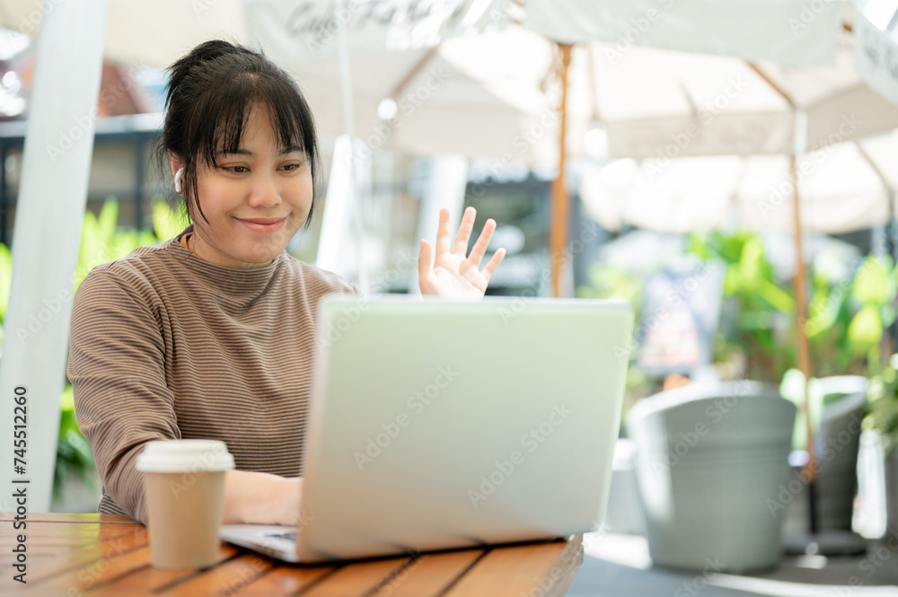 A positive Asian businesswoman is working remotely at a cafe, having an online meeting with her team
