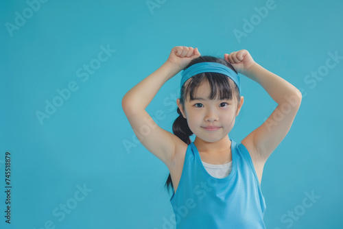 young fitness Asian athletic sport little girl doing sport, showing strength gesture with arms, blue background