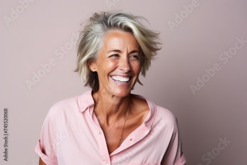 Portrait of a happy senior woman smiling on a pink background.