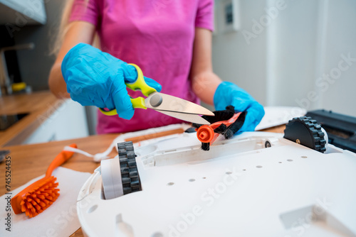 A young woman cleans a robot vacuum cleaner from dirt after cleaning.