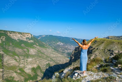 Elegant Young Woman Admiring Scenic Mountain and Lake View in Blue Dress