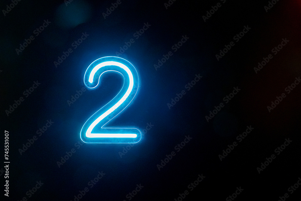 Naklejka premium Number two glowing on the dark background. Close up of bright number 2