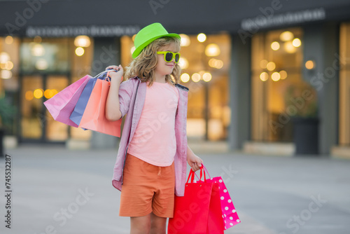 Kid with many shopping bags outdoor. Cute little boy in summer fashion kids clothes with shopping bags walking on street.