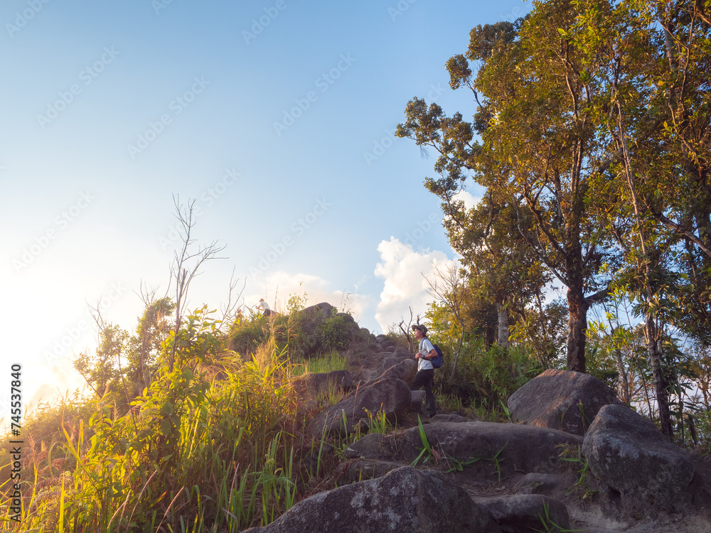 Obraz premium Asian man with backpack traveling solo on a tropical mountain peak in the sunset