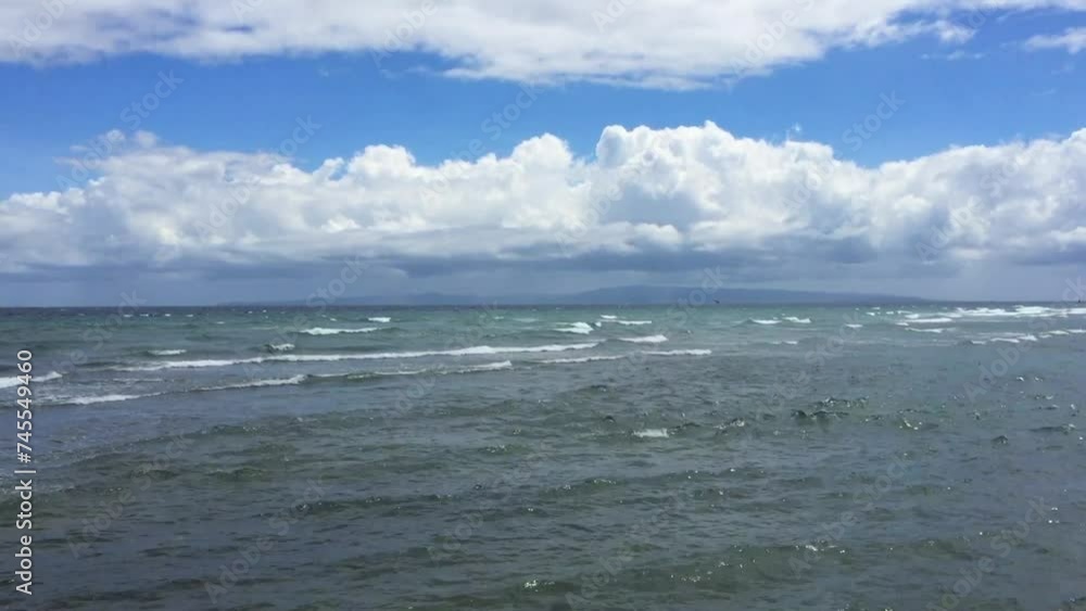 The waves are crashing in from the ocean to the beach in Dumaguete Philippines. Heavy clouds in the blue sky. A sunny day on the beach on a tropical island in Asia. The waves are crashing in from the ocean to the beach in Dumaguete Philippines. Heavy clouds in the blue sky. A sunny day on the beach on a tropical island in Asia.