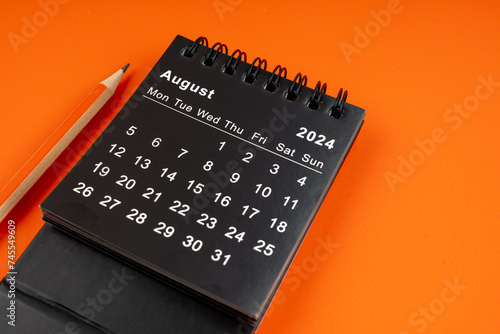 August 2024 desk calendar with pencil on orange background.