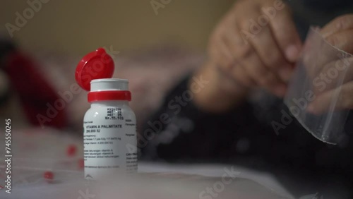 Nurse hands put Vitamin A supplement capsule in to plastic packaging. Close up selective focus photo