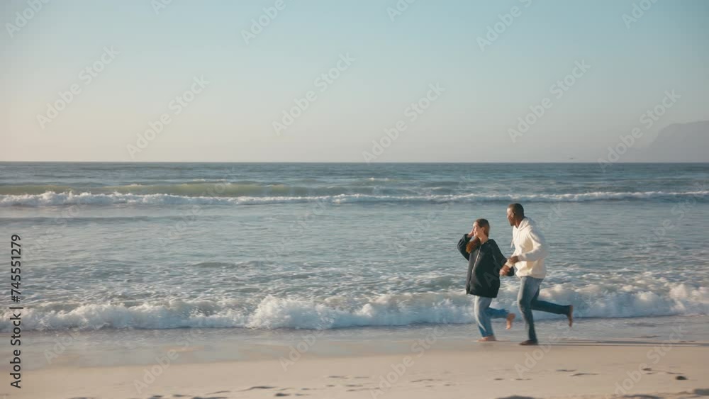 Camera tracks full length shot of casually dressed loving young couple running hand in hand along sandy shoreline of beach and sea in South Africa - shot in slow motion Camera tracks full length shot of casually dressed loving young couple running hand in hand along sandy shoreline of beach and sea in South Africa - shot in slow motion
