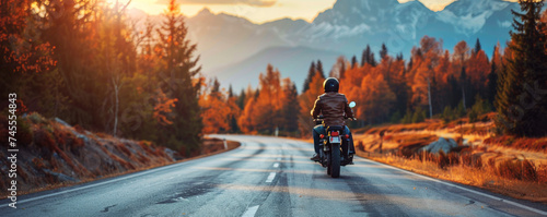 Motorcyclist Riding Through Autumn Forest. A lone motorcyclist on a scenic road surrounded by autumn forest and mountains.