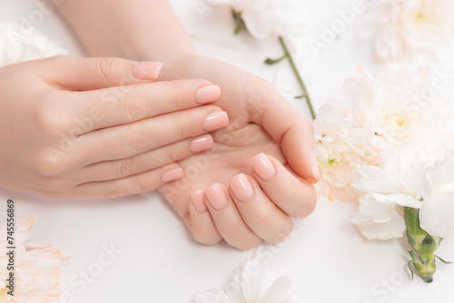 Stylish trendy nail young woman hands pink manicure on white background with flowers, top view