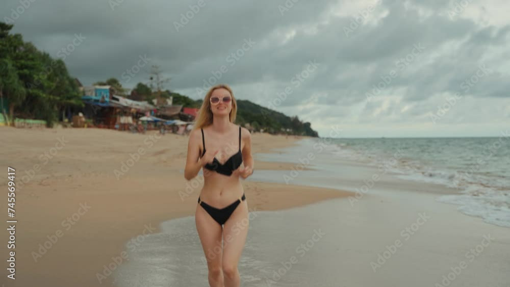 A blonde girl wearing a black bikini running on a white sandy beach. Slow motion shot. A blonde girl wearing a black bikini running on a white sandy beach. Slow motion shot.