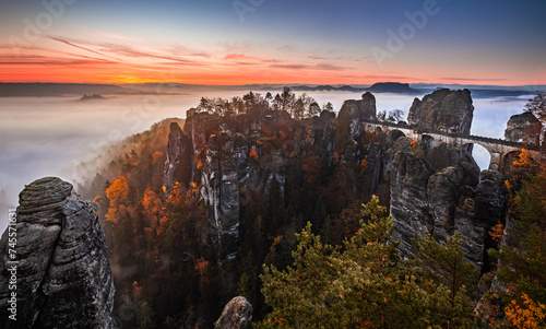 Saxon  Germany - Panoramic view of the Bastei bridge on a sunny autumn sunrise with colorful foliage and heavy fog under the valley. Famous for the rock formation in Saxon Switzerland National Park