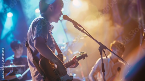 Asian musician playing guitar and singing into microphone on stage with band