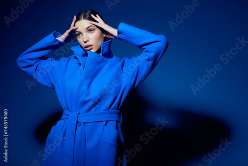 fashion portrait of young elegant woman in blue coat on blue background