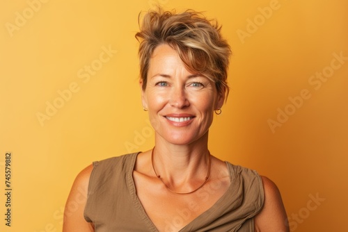 Portrait of smiling middle aged woman with short hair on yellow background © Iigo