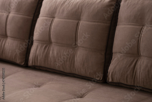 Close-up of stitched quilted plump soft pillows on a beige-brown sofa. Upholstered furniture made of combined velor fabric with a blurred background.