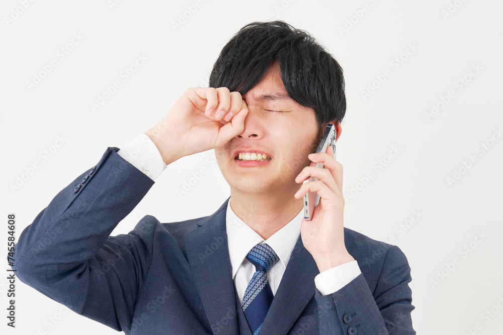 泣きながらスマートフォンで電話するビジネスマン　白背景