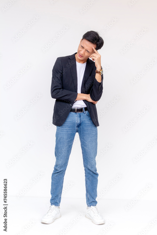 A pensive young adult stands with a slight smile, touching his temple, wearing business casual attire against a white background. A pensive young adult stands with a slight smile, touching his temple, wearing business casual attire against a white background.