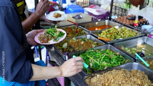 Counters with a lot of Thai dishes. A variety of exotic Asian dishes on the street, various types of dishes selling at the food stall, people can seen choosing the dishes at the stall photo