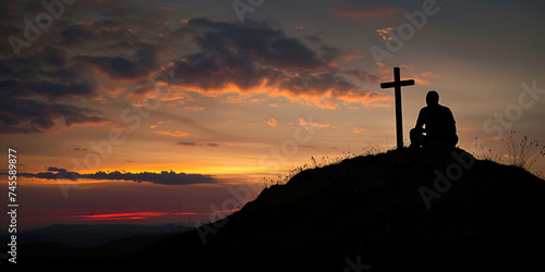 Regretting sins, missing people who passed away, deeply religious person, praying, thinking about soul and meaning of life. Silhouette of a man sitting on high hill with cross during sunrise or sunset