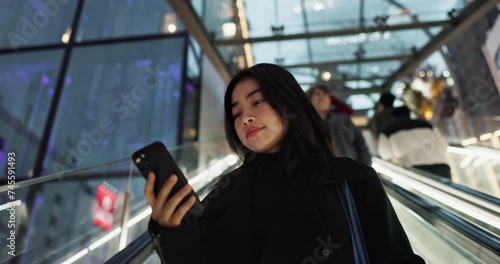 Japanese woman on city escalator with phone, internet and connection on morning commute. Search, schedule and travel, Asian girl in mall checking email or post on smartphone app on journey in Tokyo. photo