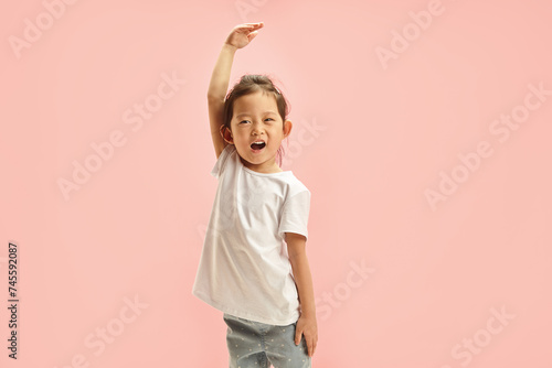 Canvastavla Cheerful Asian ethnicity little girl playfully stretches arm upwards, showing he