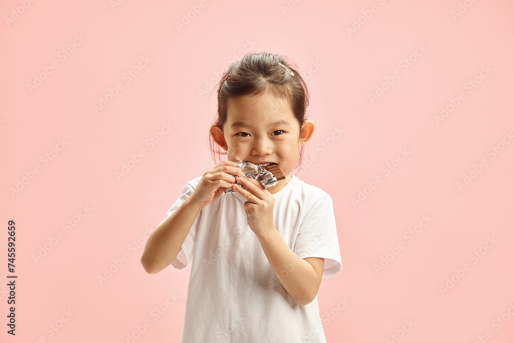 Portrait of Sweet Child Girl in White t Shirt Biting Greedily Chocolate Bar Isolated on Pink Background Portrait of Sweet Child Girl in White t Shirt Biting Greedily Chocolate Bar Isolated on Pink Background