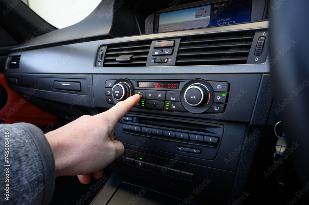 Hand pressing the auto climate control button on a car centre console