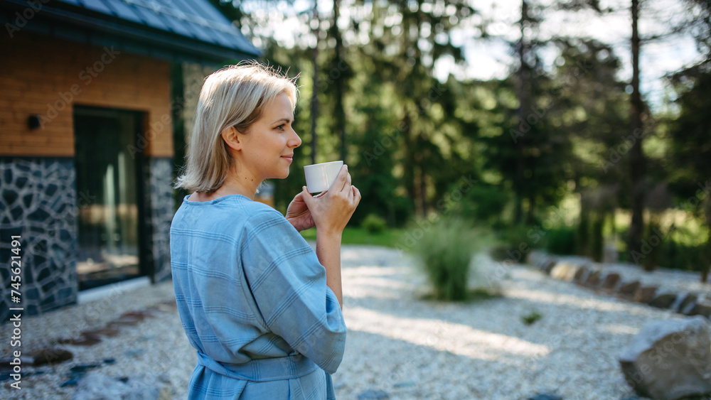 Happy young woman standing in garden near cottege and enjoying cup of morning coffee on summer vacation in mountains. Happy young woman standing in garden near cottege and enjoying cup of morning coffee on summer vacation in mountains.
