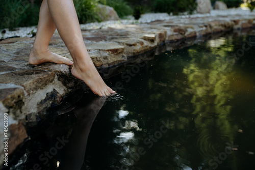 Quadro em tela Unrecognizable young woman is dipping her foot in cool water of pond, refreshing and hardening concept