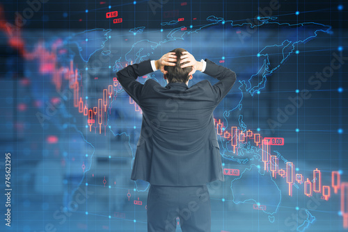 A businessman with head in hands standing before a futuristic screen displaying world maps and financial data indicating a global economic downturn