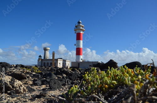 The 19th century red and white bands Faro del Tostón lighthouse located on the northwest coast of Fuerteventura in the Canary Islands. A lighthouse against the background of the blue sky and the ocean