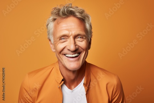 Handsome mature man looking at camera and smiling while standing against orange background © Iigo