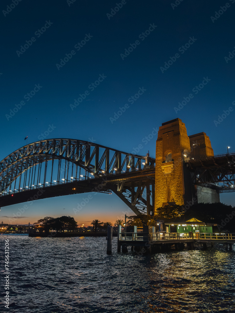 Fototapeta premium Sydney by night and at sunset is a beautiful sight to behold. The city skyline, complete with the iconic Harbour Bridge, is a picture-perfect view of Australia.