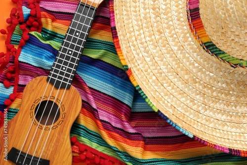 Mexican sombrero hat, guitar and colorful poncho on orange background, flat lay