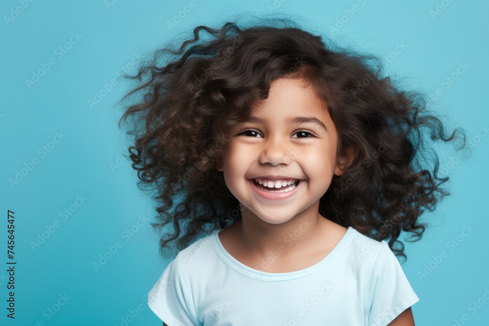 Closeup portrait of a happy little girl with curly hair, isolated on blue background Closeup portrait of a happy little girl with curly hair, isolated on blue background