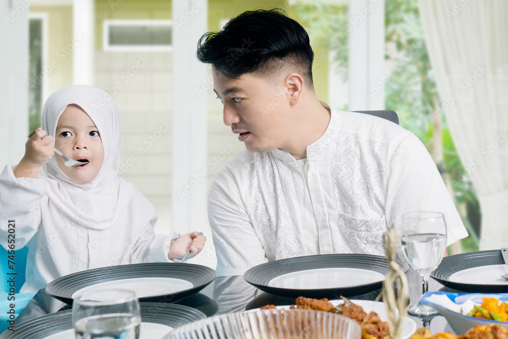 Father talking to his cute daughter wearing hijab at dining table Father talking to his cute daughter wearing hijab at dining table