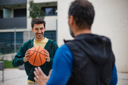 Best friends playing sport outdoors, having fun, competing. Playing basketball at a local court, enjoying exercise together. Concept of male friendship, bromance.
