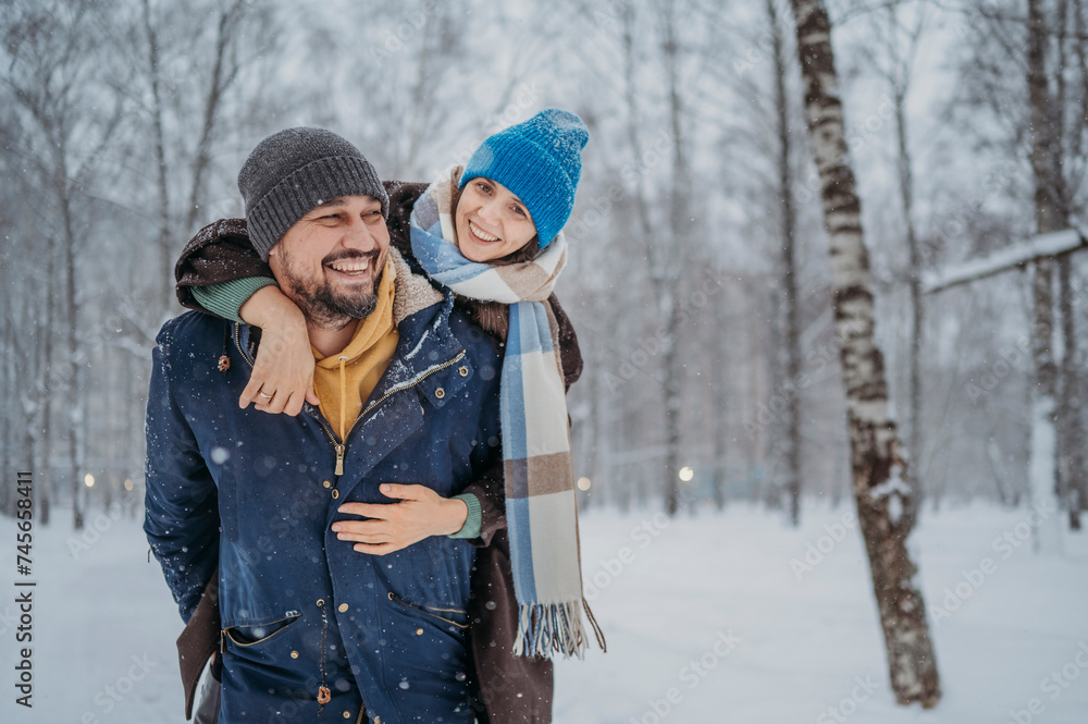 Happy man giving piggyback to woman at park in winter Happy man giving piggyback to woman at park in winter