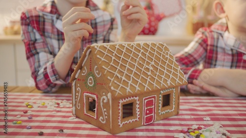 Cute boys decorating gingerbread house with topping and icing at the kitchen