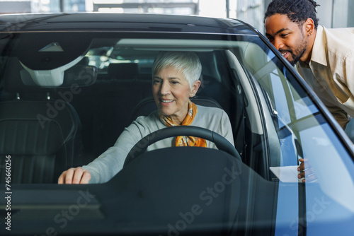 Smiling salesperson with woman examining car in showroom photo