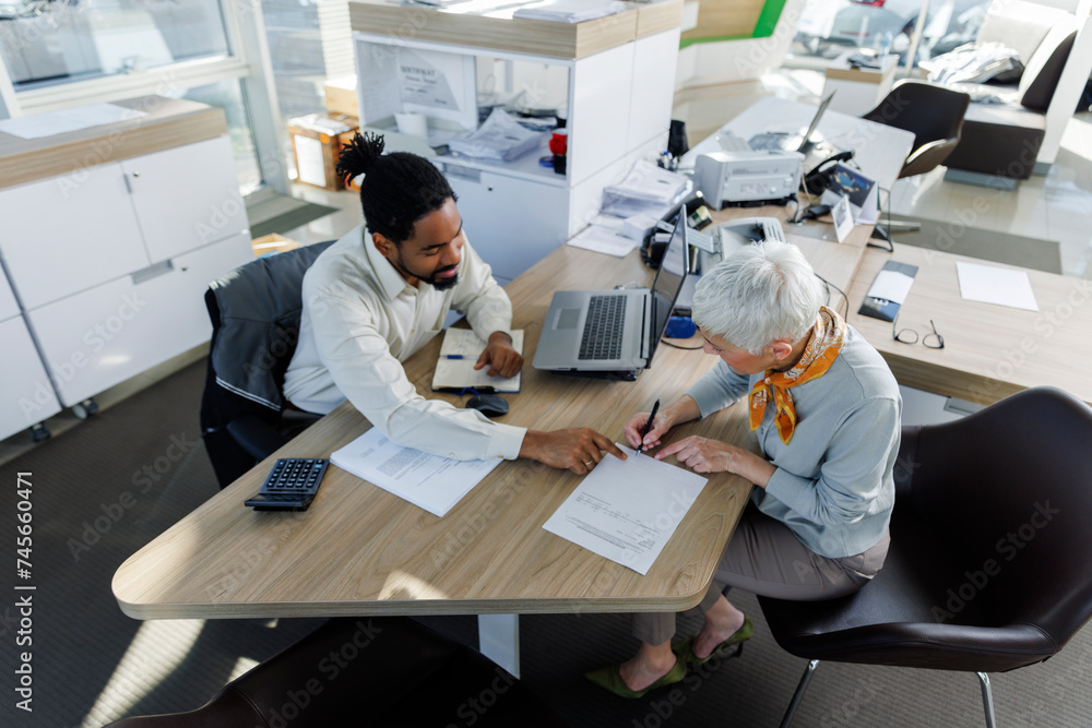 Senior woman signing contract with salesperson sitting at desk Senior woman signing contract with salesperson sitting at desk