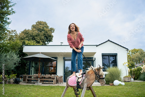 Cheerful woman standing on wooden horse in front of house photo