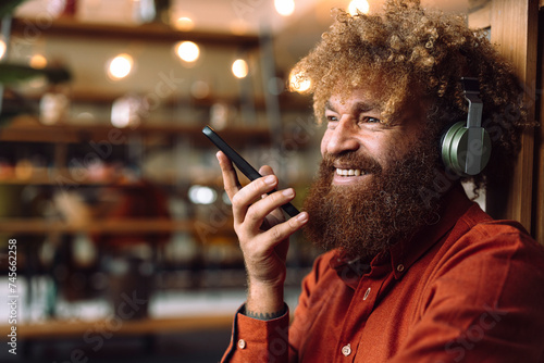 Smiling businessman wearing wireless headphones listening to music and holding smart phone photo