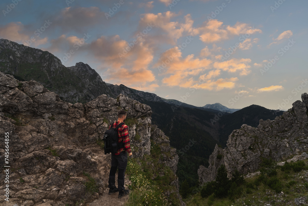 Male traveler landscape photographer with a briefcase behind his back in the Polish Tatras at sunset.