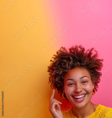 Cheerful, positive African American woman with afro hair showing an idea gesture, smiling and looking at the camera, pink and yellow background, copy space for your promotion or text message