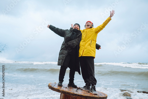 Cheerful friends standing with arms outstretched on wooden spool at beach photo