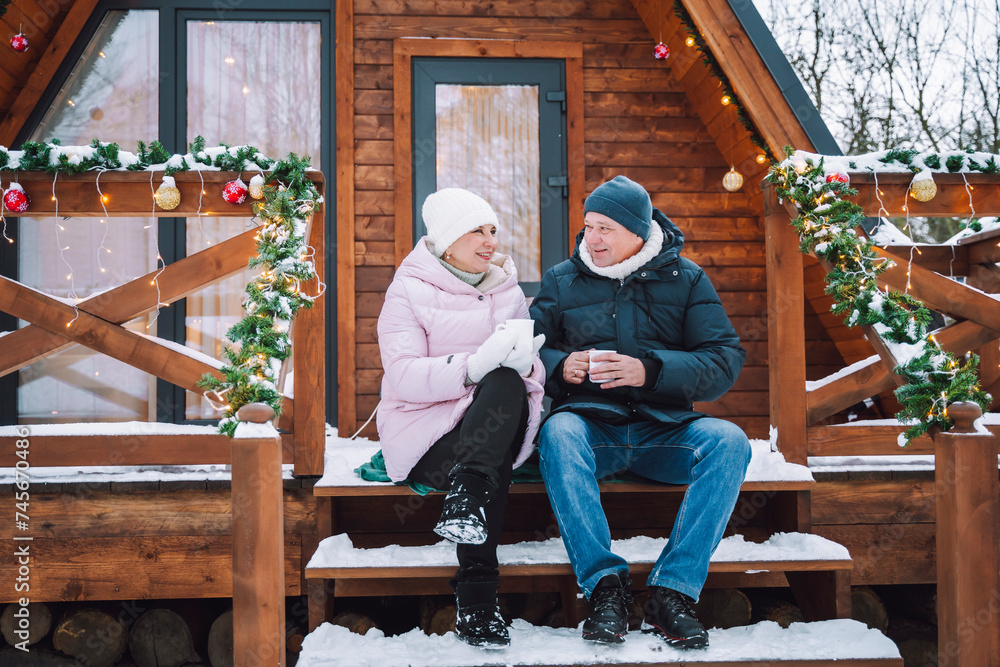 Mature couple sitting and having tea on porch near log cabin Mature couple sitting and having tea on porch near log cabin